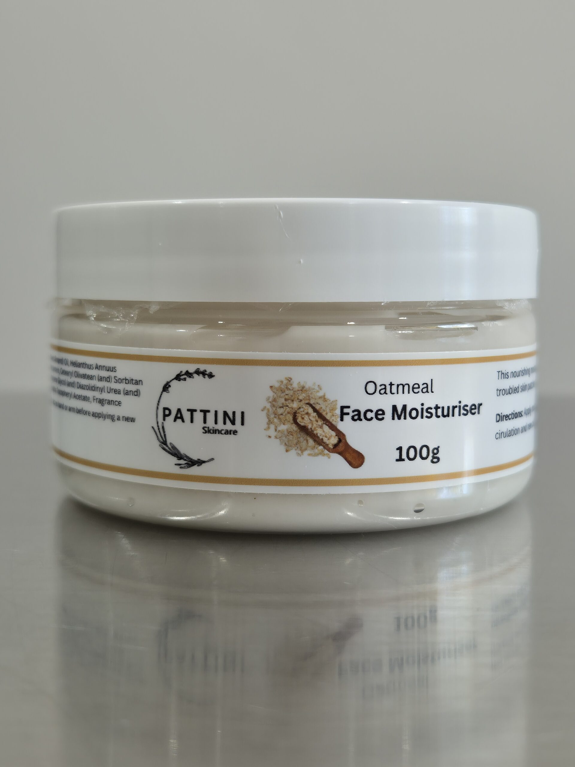 A white jar of Pattini Skincare Oatmeal Face Moisturiser with a beige label featuring an oatmeal graphic, placed on a reflective surface.