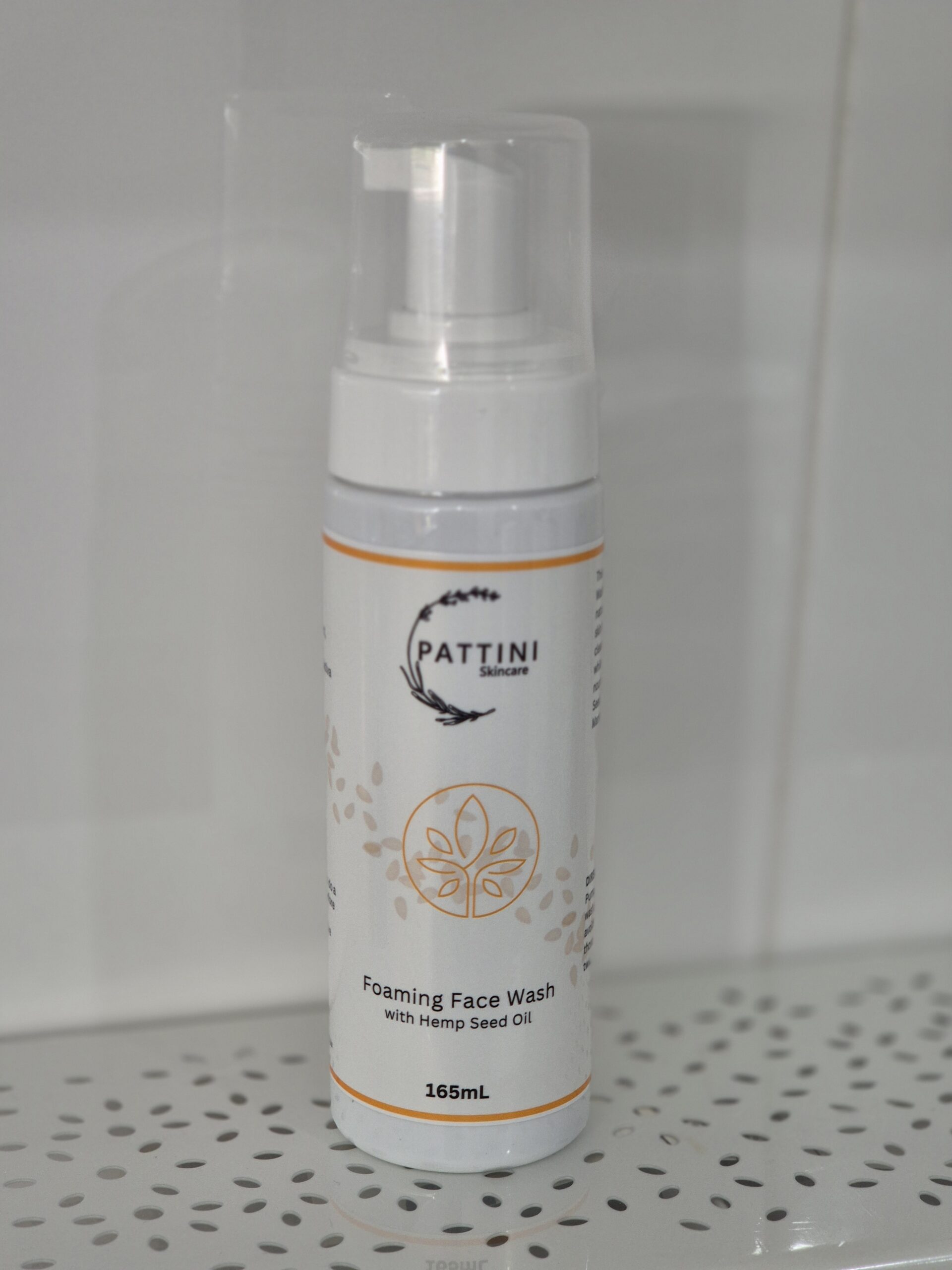 A white pump bottle of Pattini Skincare Foaming Face Wash with Hemp Seed Oil, placed on a perforated shelf against a tiled background.