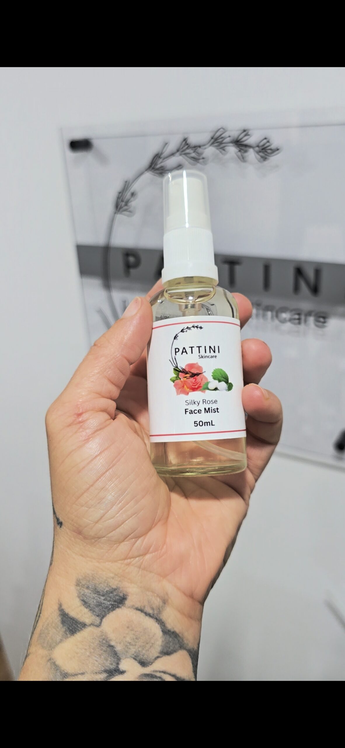 A hand holding a clear spray bottle labeled Silky Rose Face Mist 50mL from Pattini Skincare.